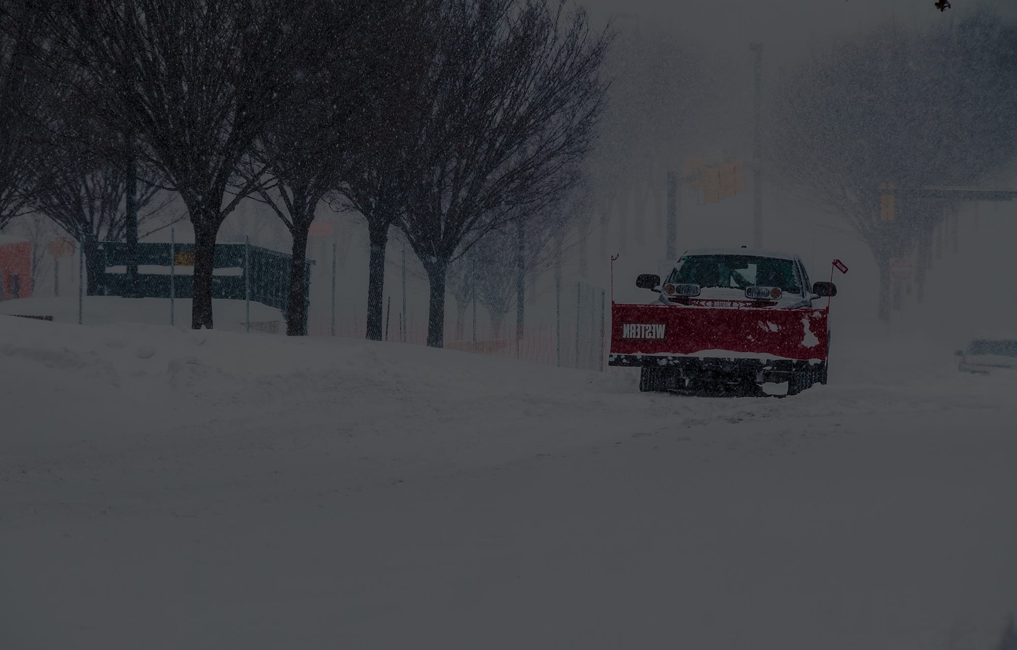 Plow truck clearing a commercial parking area during a snowstorm in South Portland, Maine